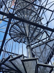 Steel structure of an observation tower with spiral stairs, against a blue sky background. Close up.