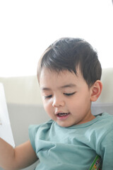 Obraz premium Little boy reading a book in the living room interior at home. Prepare to come back to school.