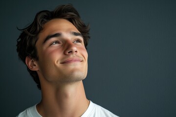 Fototapeta premium Smiling young man daydreaming against a dark gray background with ample copyspace for text, showcasing a sense of hope and contemplation.