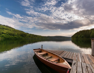 Fototapeta premium a serene landscape featuring a small boat docked at a wooden pier by a calm lake under a cloudy sky