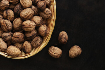 Walnuts in a wicker basket on a dark wooden background. Nuts in an oval basket, top view. Heap of...