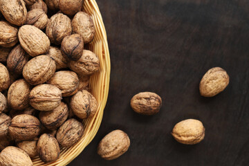 Walnuts in a wicker basket on a dark wooden background. Nuts in an oval basket, top view. Heap of...