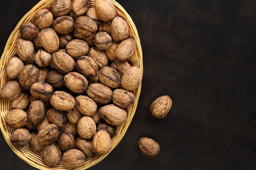 Walnuts in a wicker basket on a dark wooden background. Nuts in an oval basket, top view. Heap of...