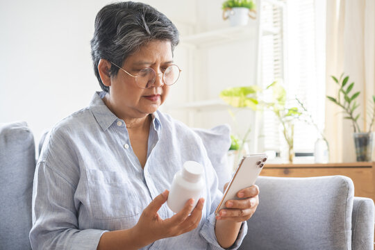 Health care concept, asian senior woman using smart phone reading, searching prescription on bottle medicine, pill label text about information online, instructions side effects, pharmacy medicament.