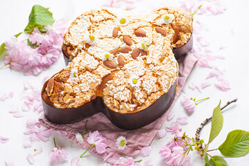 Сolomba pasquale - Italian sweet Easter bread or cake with almonds and powdered sugar and candied fruits. The baked dove is a symbol of Christ and the Easter holiday, pink flowers, natural style