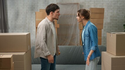 Young couple moving into new apartment, space filled with cardboard boxes, man and woman standing...