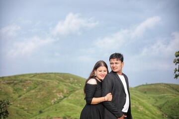 Happy young Indian couple in trendy clothes embracing against mountain under sky on sunny day
