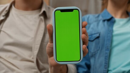 Young couple moving into new apartment, space filled with cardboard boxes, man and woman sit on the sofa with smartphone chroma key green screen.
