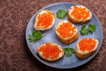 Sandwiches with red caviar on a plate decorated with cilantro on a brown tablecloth