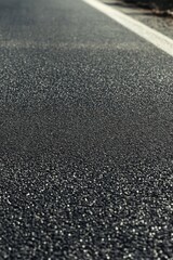 Close view of a newly paved asphalt road alongside a grassy area in daylight showing clear markings and vibrant textures
