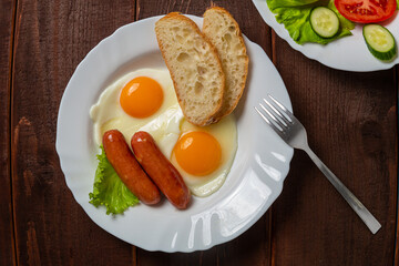 Breakfast fried eggs with sausages crispy white bread and tea on a wooden table