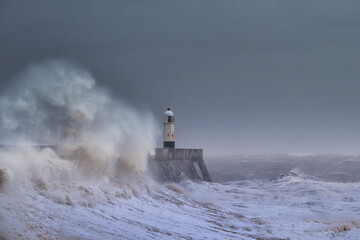 A huge winter storm hitting the coast of the UK. Giant waves crash into a breakwater, with a...