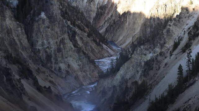 Grand Canyon of the Yellowstone, medium shot from Brink of Lower Falls on a summer evening, featuring the Yellowstone River and colorful canyon walls glowing in warm light and deep shadows.