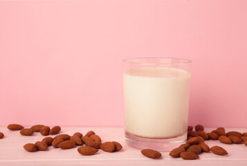 Fresh almond milk in glass and almonds on pink background. Healthy vegan plant based alternative milk replacer. Vertical photo