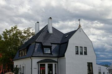 A picturesque white chapel sits beside a quiet cemetery on a grassy hill, with a tranquil fjord and towering mountains in the background. Peaceful, rural, and scenic Nordic setting.