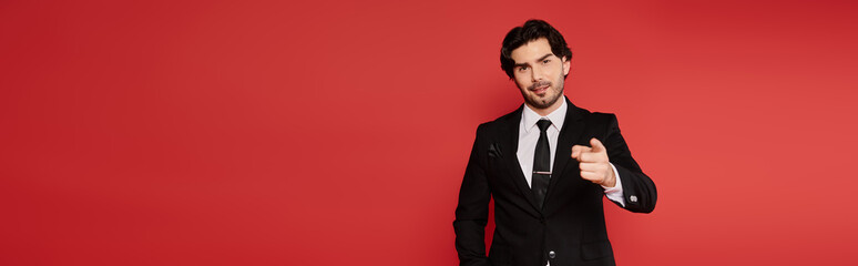 Handsome young man in a suit pointing confidently against a vibrant red backdrop
