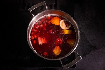 Top view of a pot filled with boiling fruit compote, featuring vibrant red berries, orange slices, and lemon slices, creating a warm and cozy atmosphere.