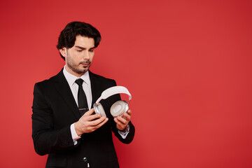 Young handsome man in a suit exploring stylish headphones against a vibrant red backdrop
