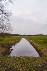Tranquil Canal Cutting Through Verdant Field with Overcast Sky