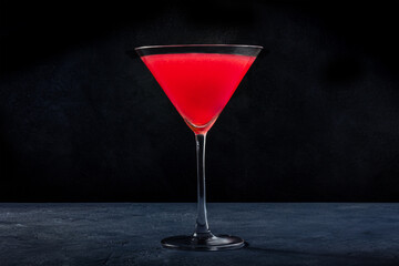 Cosmopolitan cocktail with vodka and cranberry juice in an elegant glass, on a black background