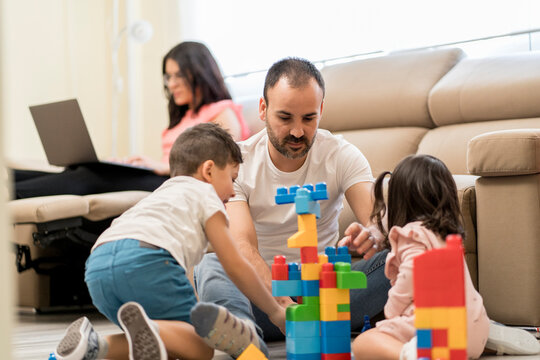 Father assembling constructor with kids near working mom