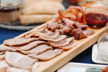 slicing of different types of meat on wooden board on table in restaurant, snacks, appetizer