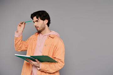 Young handsome man contemplating while holding a notebook and pen in a stylish outfit