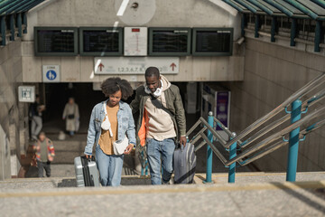 Two passengers, a man and a woman talking and walking along the train station platform rolling wheel suitcases.