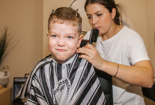 The boy is squirming while the barber cuts his hair.