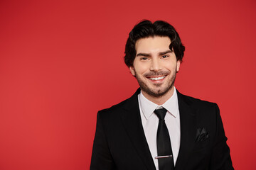 Young handsome man in a suit smiles brightly against a vibrant red background