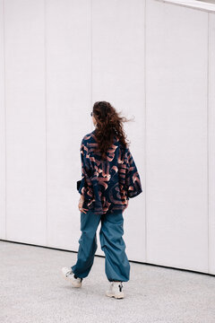 A woman in a patterned jacket and baggy pants walks along the wall