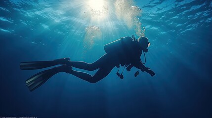 Scuba diver silhouette exploring sunlit ocean depths.