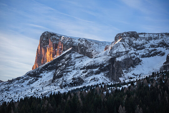 Montagne enneig&eacute;e sous les nuages d'hiver dominant une vall&eacute;e bois&eacute;e et enneig&eacute;e dans la p&eacute;nombre du soleil levant.