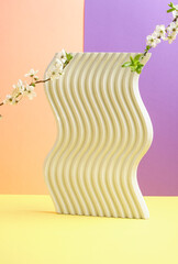 Minimalistic composition featuring a textured wavy concrete stand with blossoming branches. A modern and creative design element.