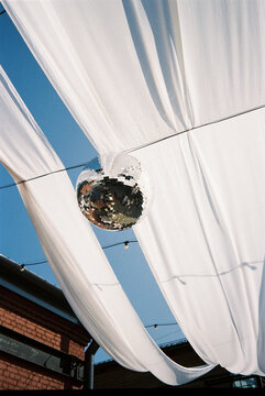 Disco ball hanging under white drapes at a festive outdoor setting