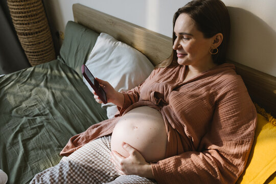 A pregnant woman with a phone in bed