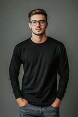 Fototapeta premium A young man wearing a black long sleeve T-shirt mockup and glasses, standing against a gray background with a neutral expression.