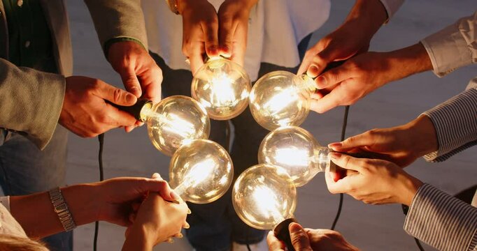 Business people group holding illuminated lightbulb joining hands in a circle sharing creative energy and innovative ideas. Teamwork, cooperation and success concept. 4l video. Slow motion video.