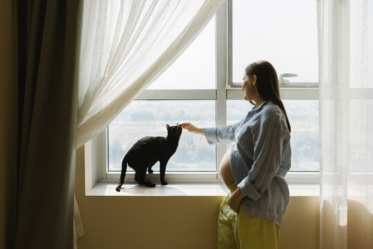 A woman sitting on the window sill with her cat