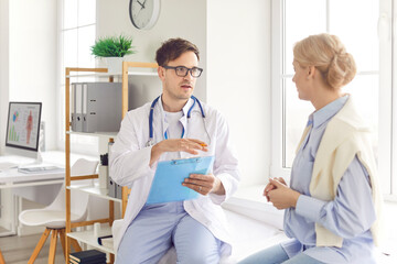 Young woman patient sitting on couch in medical office listening to friendly male doctor therapist...