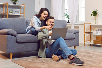 Happy overjoyed couple looking at laptop screen, sitting on cozy couch at home, smiling young woman...