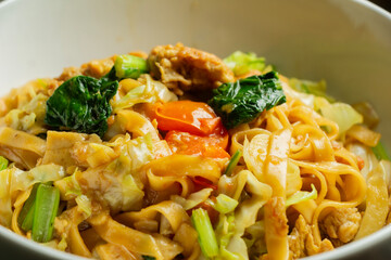Closeup of selected Thai drunken noodles with egg and sausage combination, Asian food Kwetiau in white bowl