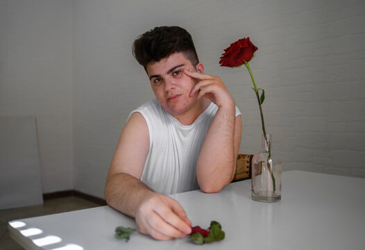 Serious non binary person sitting at the table in white studio