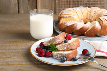 Pieces of freshly baked sponge cake, berries and milk on wooden table, closeup