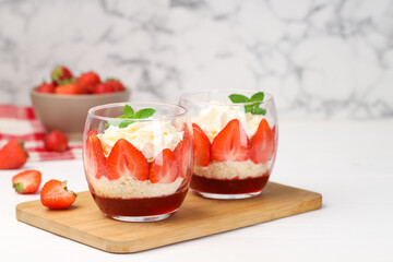 Tasty trifle dessert. Sponge cake, strawberries, jam and whipped cream in glasses on white table
