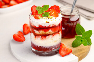 Tasty trifle dessert. Strawberries, sponge cake and whipped cream in glass on beige table