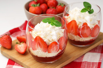 Tasty trifle dessert. Sponge cake, strawberries, jam and whipped cream in glasses on table, closeup