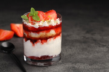 Tasty trifle dessert. Strawberries, sponge cake and whipped cream in glass on grey table, space for text