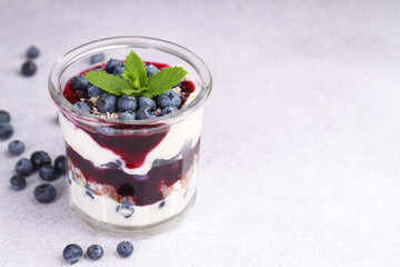 Tasty trifle dessert. Blueberries, sponge cake and whipped cream in glass on light grey table, space for text