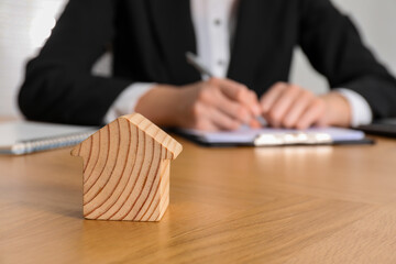Property insurance. Real estate agent working at table indoors, focus on wooden house figure